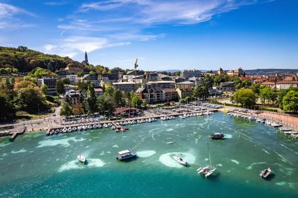 Aerial view of Annecy, France showing Lake Annecy marina, sailboats, historic architecture, and surrounding mountains on a sunny day