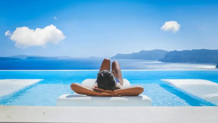 Young woman relaxing by infinity pool overlooking Aegean Sea in Santorini Greece during summer vacation
