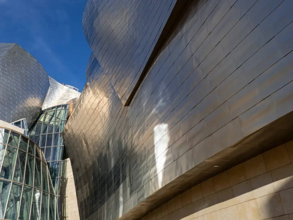 Modern architecture detail of the Guggenheim Museum Bilbao in Bilbao, Spain, showcasing reflective titanium panels and glass structure under a clear blue sky