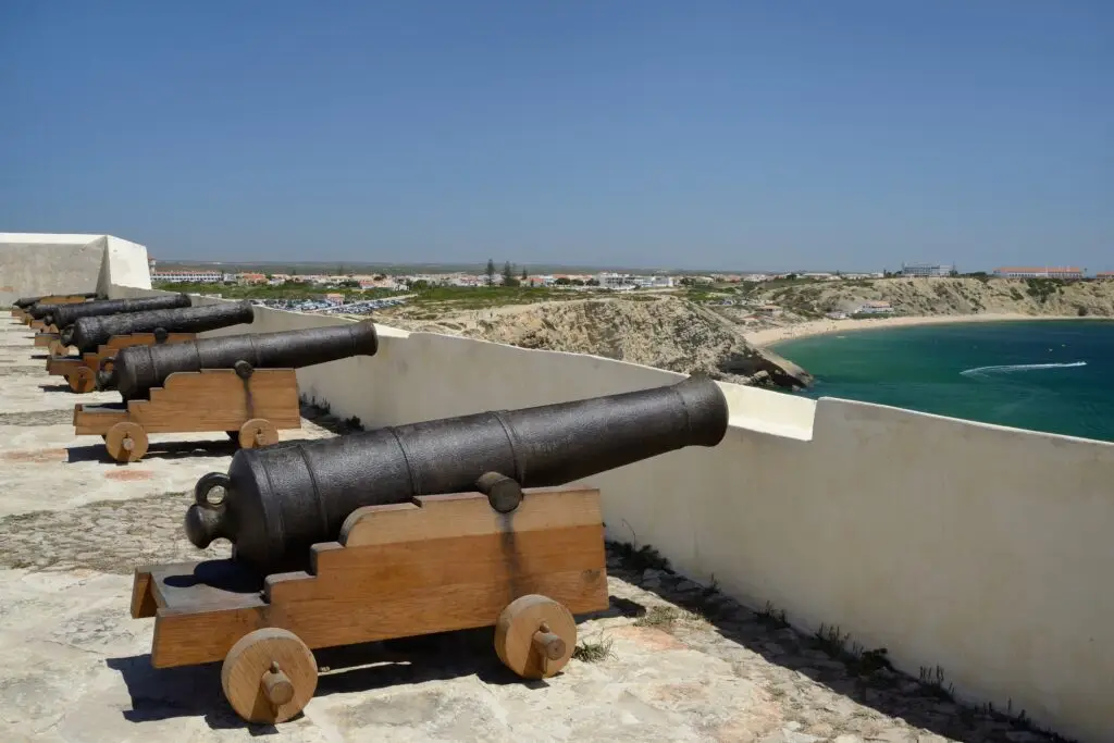 Historic cannons overlooking the Atlantic Ocean at Sagres Fort in Algarve, Portugal, with coastal cliffs and beach views in the background