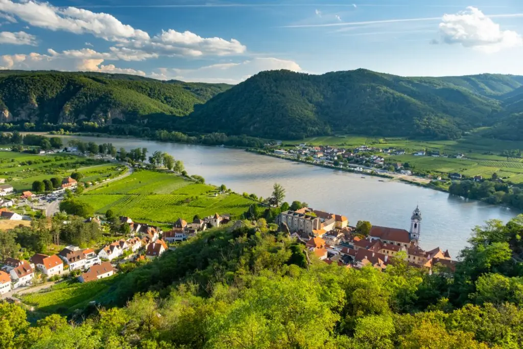 Panoramic view of Wachau Valley with the Danube River and Dürnstein village in Lower Austria, featuring vineyards, historic buildings, and lush green hills under a blue sky