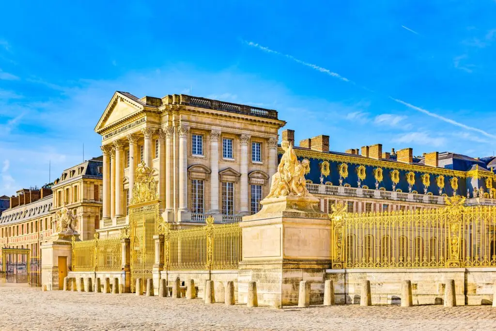 Palace of Versailles exterior with golden gates and statues under blue sky, Versailles France