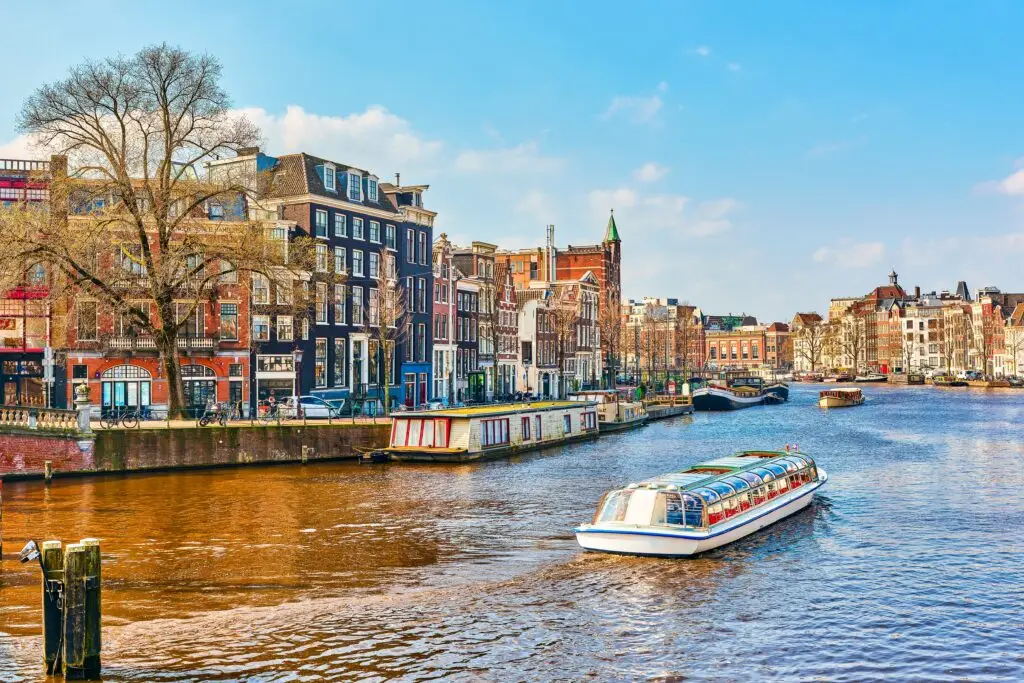 Canal cruise boat on the Amstel River with historic Dutch houses and architecture in Amsterdam, Netherlands