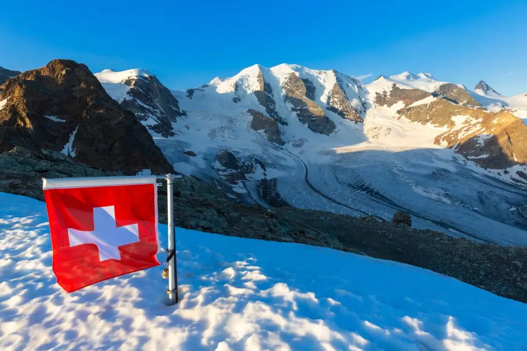 Swiss flag overlooking snow-covered mountains and glaciers at Diavolezza Refuge in the Swiss Alps, Switzerland