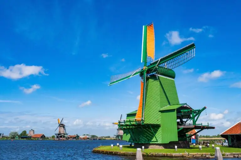 Traditional Dutch windmills at Zaanse Schans in the Netherlands on a sunny day with blue sky and water channel, popular tourist attraction near Amsterdam