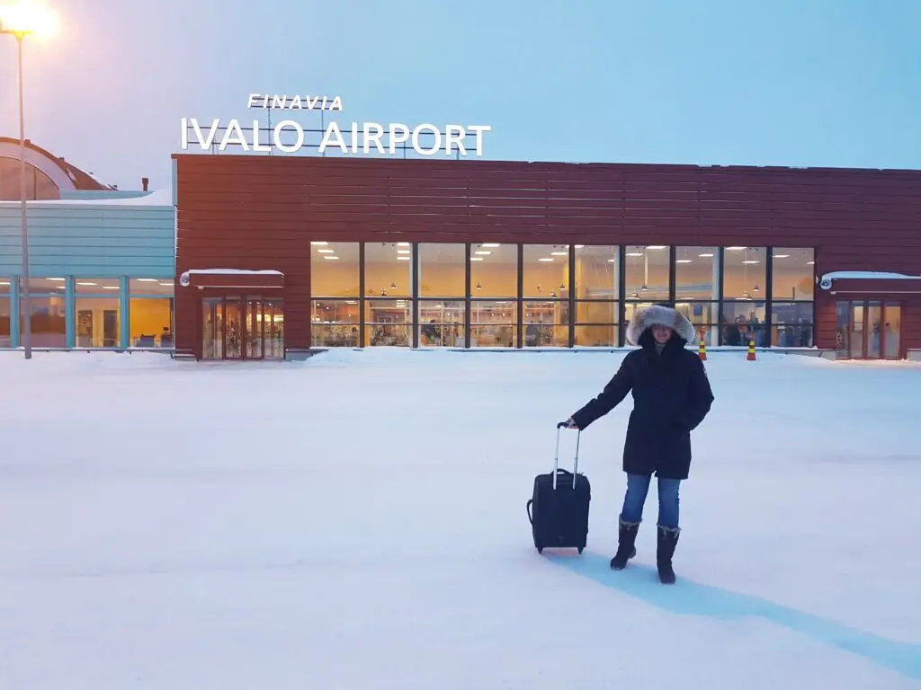 Happy young woman standing with luggage in front of Ivalo Airport in Lapland Finland during winter travel tour