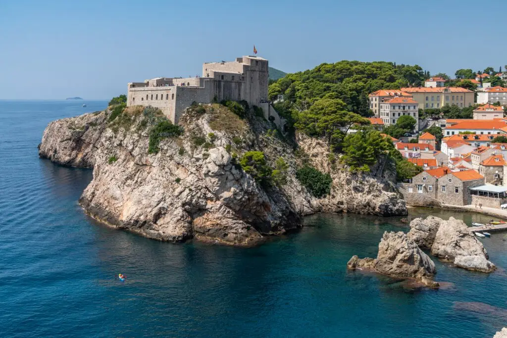 Fort Lovrijenac overlooking the Adriatic Sea near Dubrovnik, Croatia, with historic stone walls, rocky cliffs, and orange-roofed houses below, a popular tourist attraction on the Dalmatian Coast