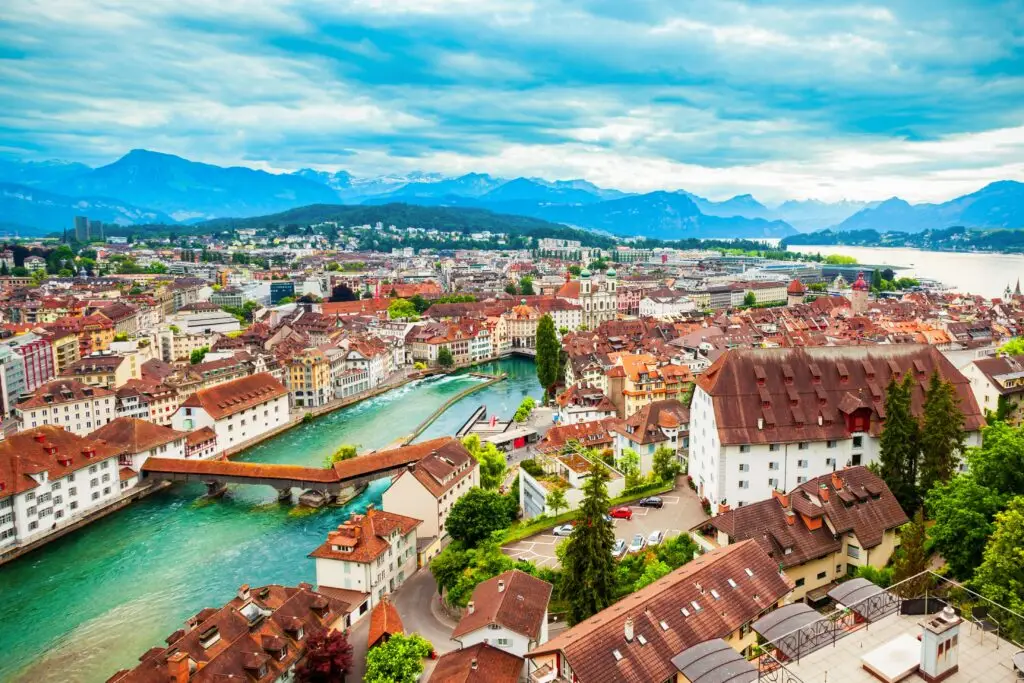 Panoramic view of Lucerne Switzerland with historic buildings, red rooftops, Chapel Bridge over the Reuss River, and scenic Alps in the background