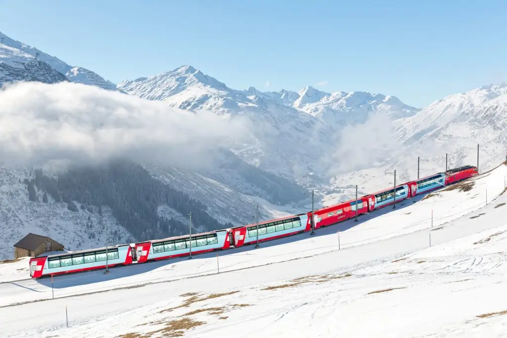 Scenic red panoramic train traveling through snowy Swiss Alps near St. Moritz, Switzerland, with mountains and winter landscape in the background