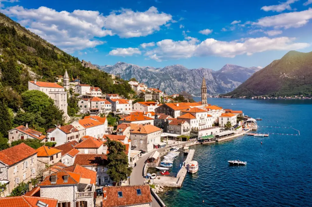 Scenic view of Perast Montenegro with historic stone buildings red rooftops church tower and Bay of Kotor surrounded by mountains and blue Adriatic Sea