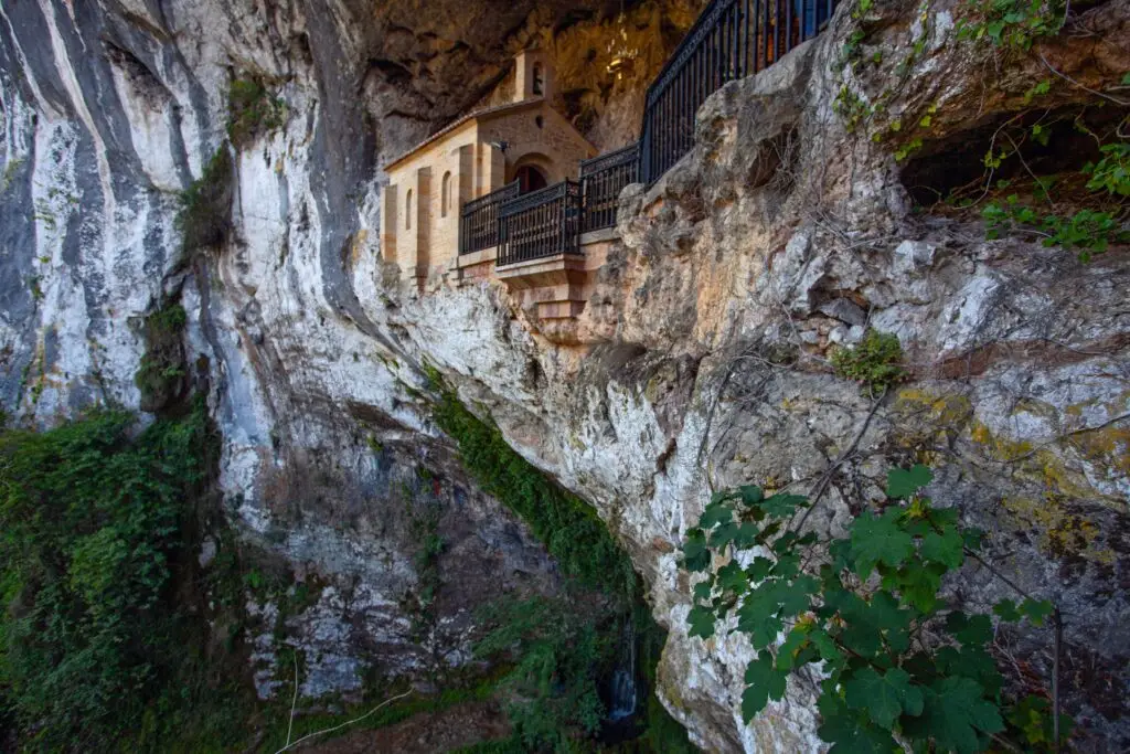 Chapel of Covadonga built into a cliffside in Asturias, Spain, surrounded by rocky landscape and greenery, a popular pilgrimage and tourist attraction in Northern Spain