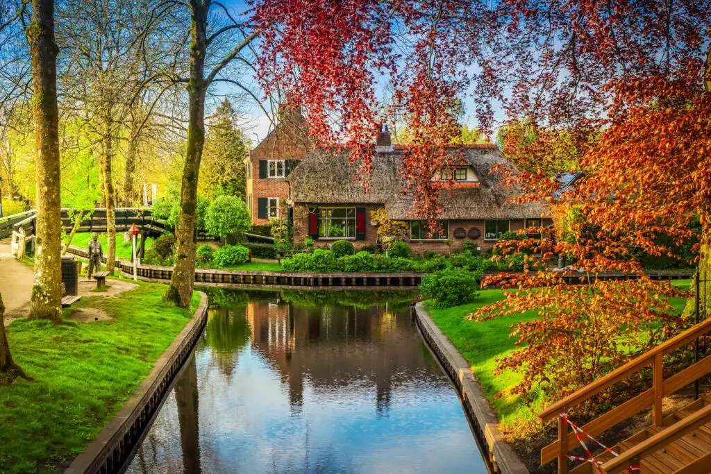 Scenic canal view in Giethoorn, a traditional Dutch village with thatched cottages, wooden bridges, and vibrant trees in the rural Netherlands countryside