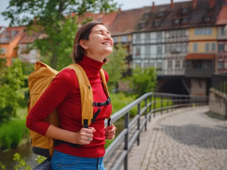 Smiling tourist woman with backpack exploring the historic city of Erfurt, Germany, enjoying a sunny day while walking along cobblestone streets near traditional German architecture