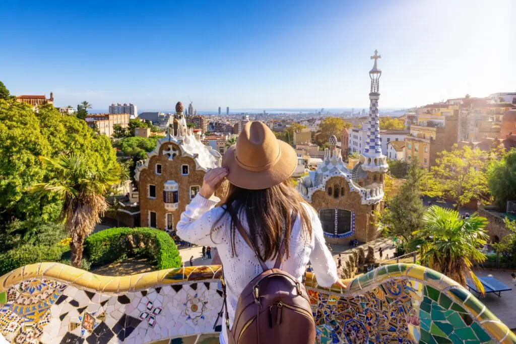 Tourist woman enjoying a sightseeing trip at Park Güell in Barcelona Spain with city skyline and colorful mosaic architecture in view
