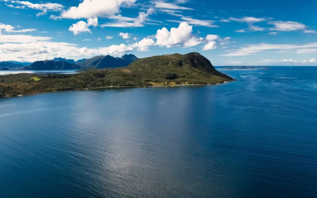 Scenic aerial view of Helgeland coastline in Norway with blue sea, lush green hills, and distant mountain landscape under a bright sky