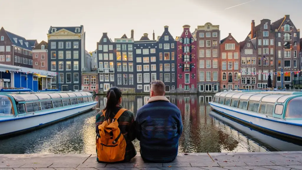 Couple sitting by the canal overlooking traditional Dutch houses and canal boats in Amsterdam, Netherlands