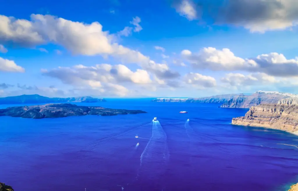 Aegean Sea and panoramic view of Santorini Caldera with boats cruising near volcanic islands, Greece tourism destination