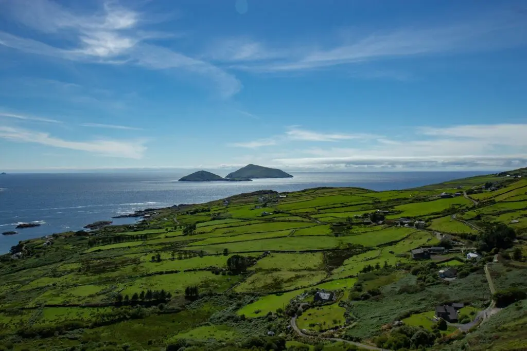 Scenic view of the Ring of Kerry in Ireland with lush green fields, coastal cliffs, and the Atlantic Ocean under a bright blue sky