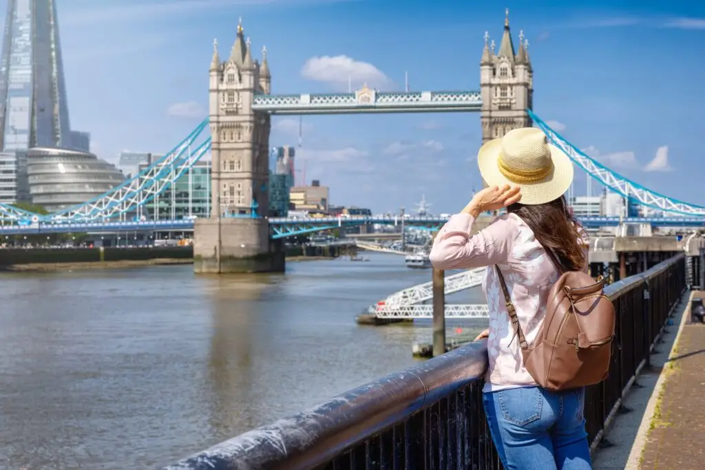 Tourist woman wearing a hat and backpack looking at Tower Bridge in London on a sunny summer day