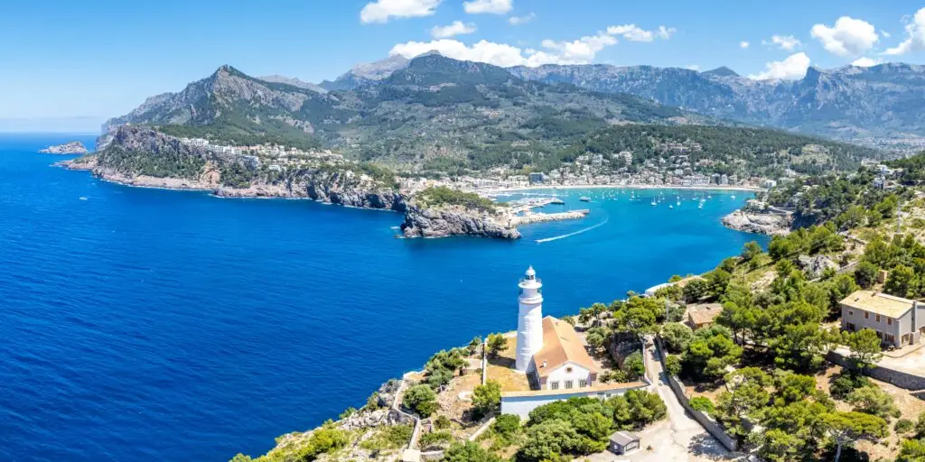 Aerial view of Port de Sóller on Mallorca Island, Spain, featuring the scenic coastline, turquoise Mediterranean Sea, and historic lighthouse surrounded by mountains and lush greenery