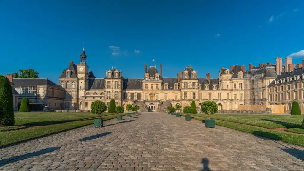 Château de Fontainebleau in France with its grand Renaissance architecture, cobblestone courtyard, and landscaped gardens under a clear blue sky