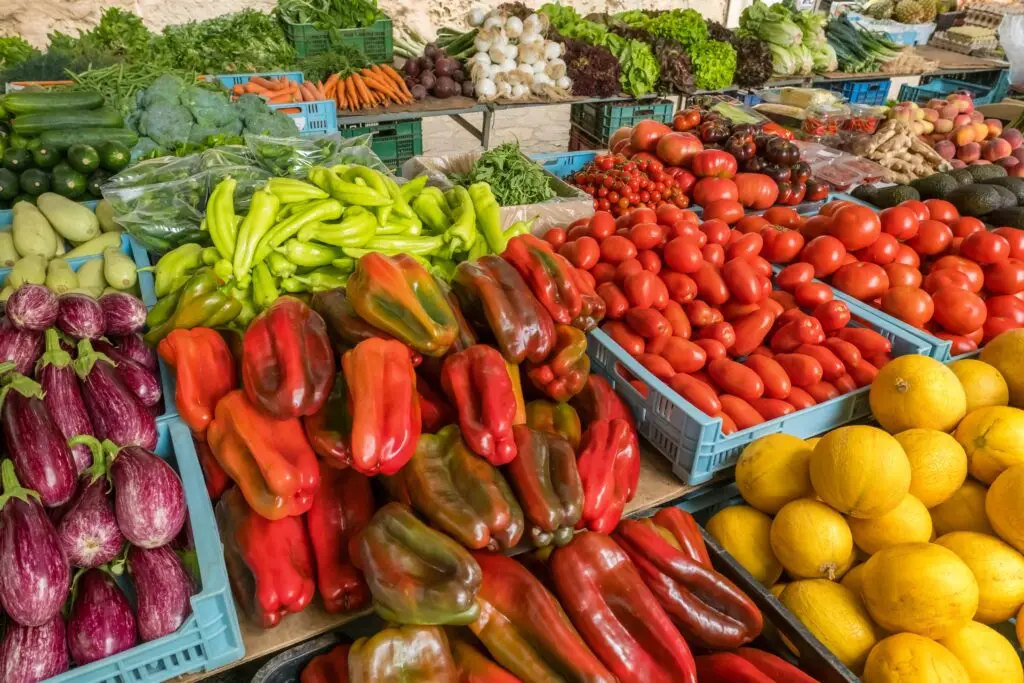 Colorful fresh vegetables and fruits on display at a farmers market in Majorca, Spain, featuring peppers, tomatoes, melons, and local produce