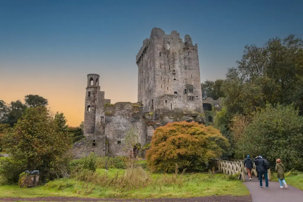 Exterior view of Blarney Castle, a historic medieval fortress in County Cork, Ireland, surrounded by lush gardens and visited by tourists at sunset