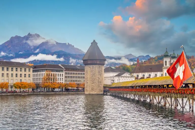 Scenic view of Chapel Bridge and Water Tower in Lucerne Switzerland with Swiss flag and mountains in the background