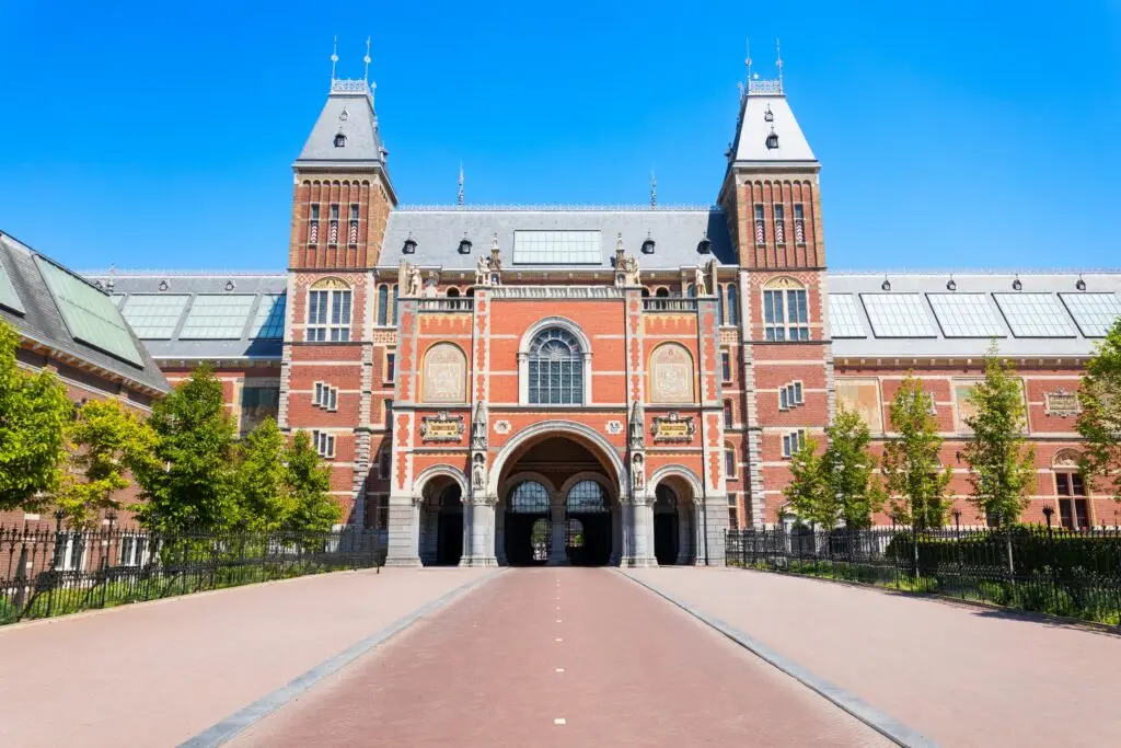 Historic Rijksmuseum building with red brick facade and archway entrance under blue sky in Amsterdam, Netherlands
