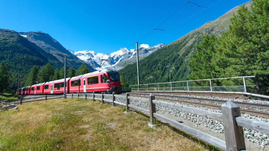 Red scenic train traveling through Bernina Pass in the Swiss Alps, Switzerland, surrounded by mountains and forests on a bright summer day