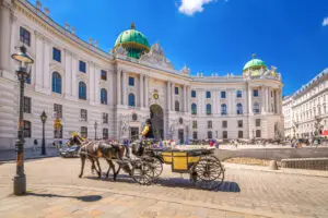 Horse-drawn fiacre carriage in front of the historic Hofburg Palace in Vienna, Austria, on a sunny day with tourists exploring the square