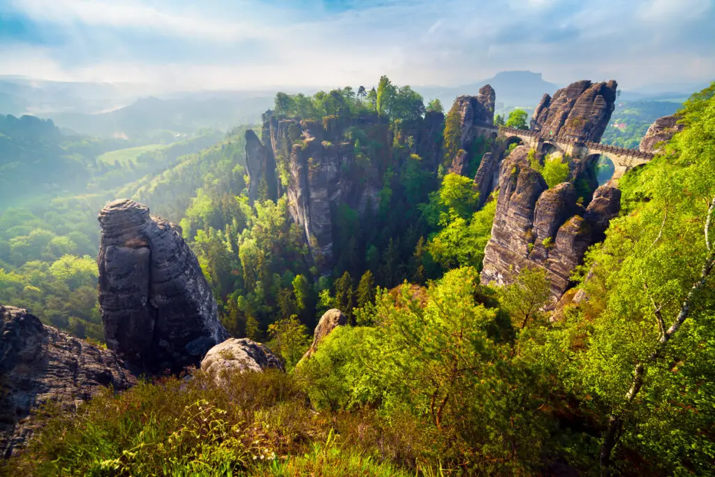 Misty morning view of the Bastei Bridge and sandstone cliffs in Saxon Switzerland National Park, Germany, surrounded by lush green forest and scenic valley landscape