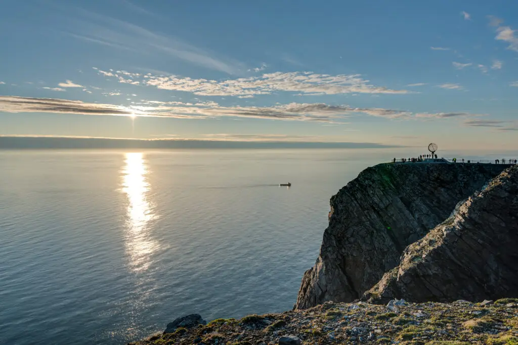 Sunset view over the Arctic Ocean from the North Cape cliff in Norway with visitors at the globe monument, a popular European travel destination