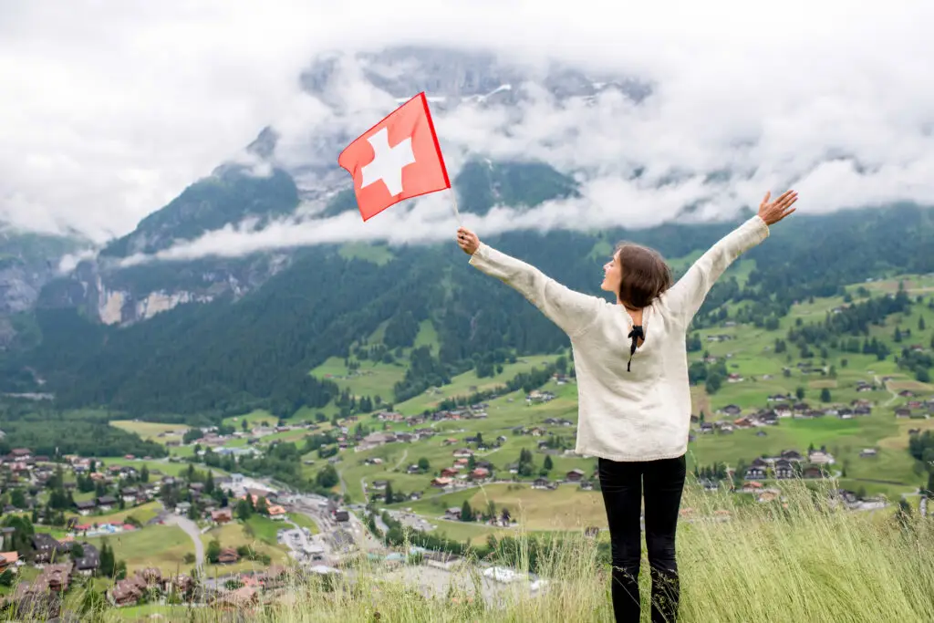 Woman holding Swiss flag overlooking the scenic alpine village of Grindelwald, Switzerland with mountains and valley views