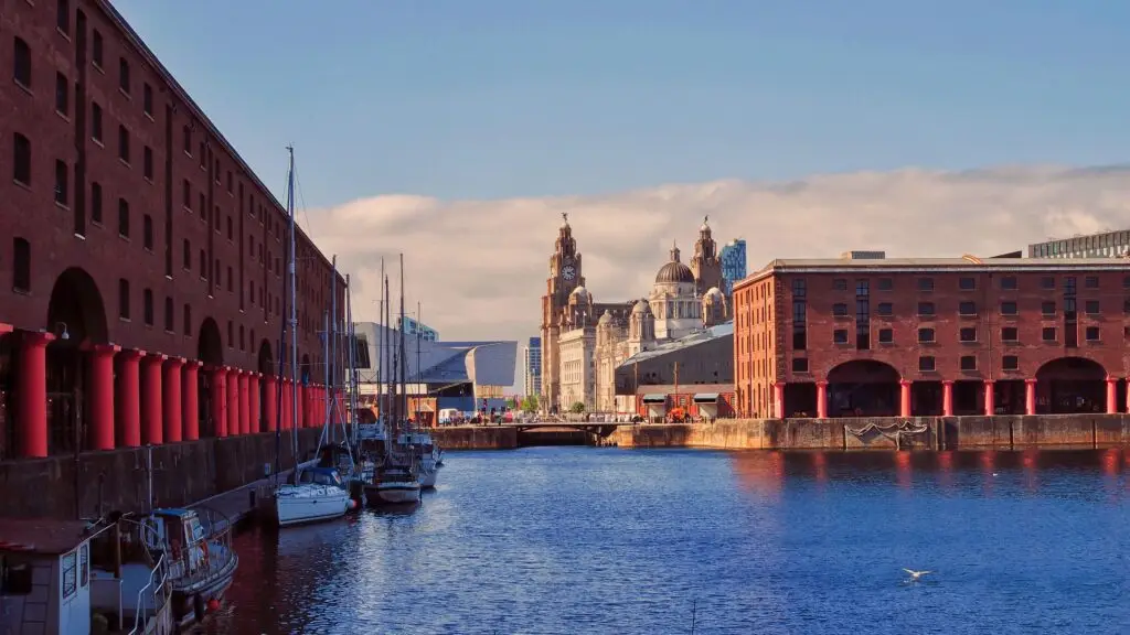 Albert Dock waterfront with historic brick warehouses, boats, and view of the Royal Liver Building in Liverpool UK