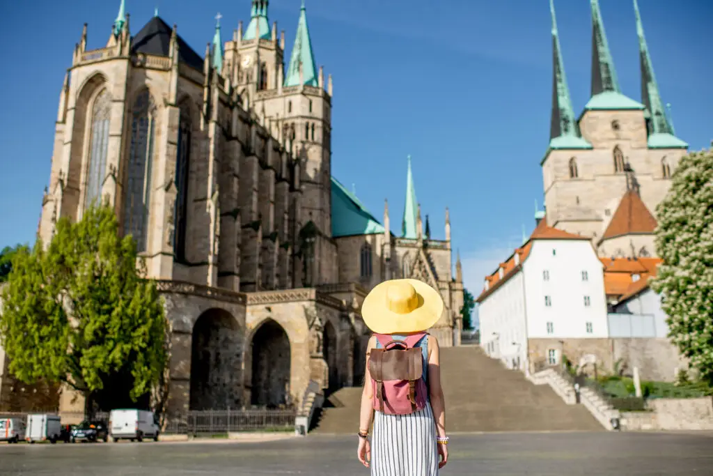 Woman tourist with backpack and yellow hat admiring the morning view of Mary Domberg Cathedral in Erfurt, Germany during a European private tour