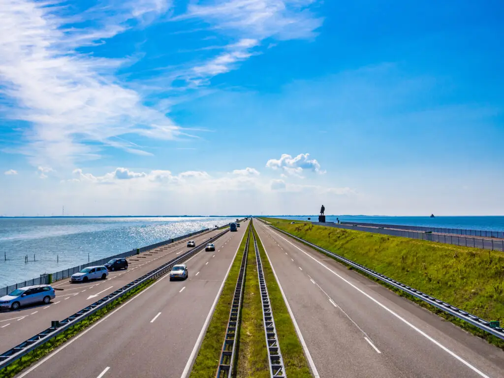 Scenic road on the Afsluitdijk Dam in the Netherlands with cars driving between the Wadden Sea and IJsselmeer under a bright blue sky