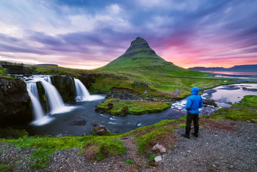 Traveler admiring Kirkjufellsfoss waterfall and Kirkjufell mountain at colorful sunset in Iceland, popular sightseeing destination on a Europe private tour