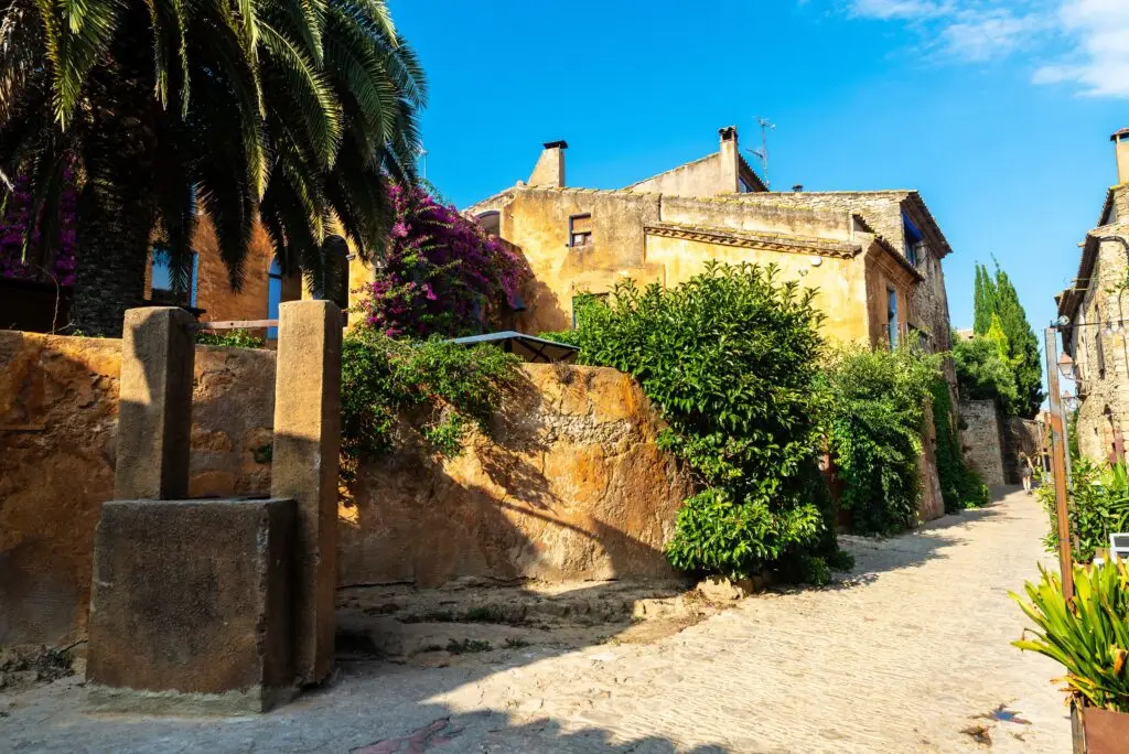 Rustic stone street with traditional Mediterranean houses and lush greenery in the historic village of Peratallada, Spain